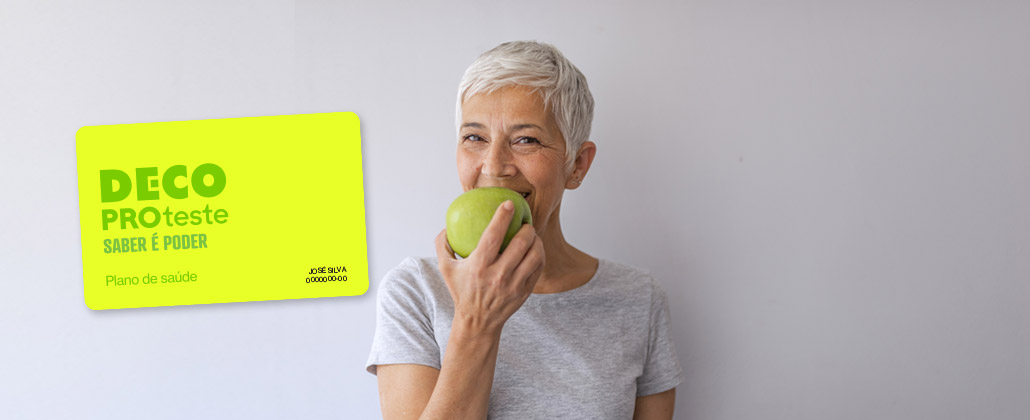 Mulher de meia idade come maçã, sorridente, ao lado da imagem do cartão da teste saúde.